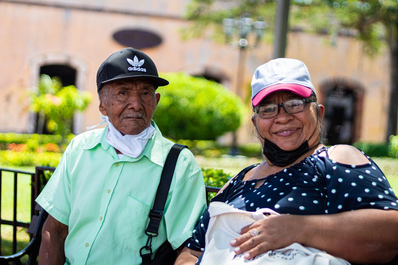 Senior couple sitting outdoors wearing face masks during daylight.