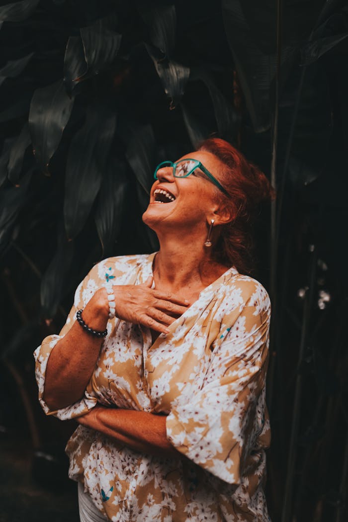 A senior woman with glasses laughing joyfully in an outdoor setting.