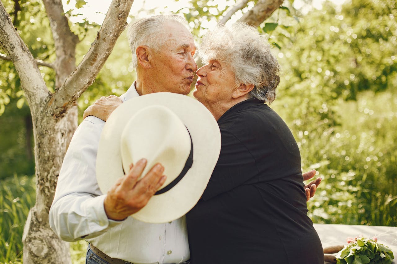 A loving elderly couple shares a tender kiss in a sunny garden, embracing each other warmly.